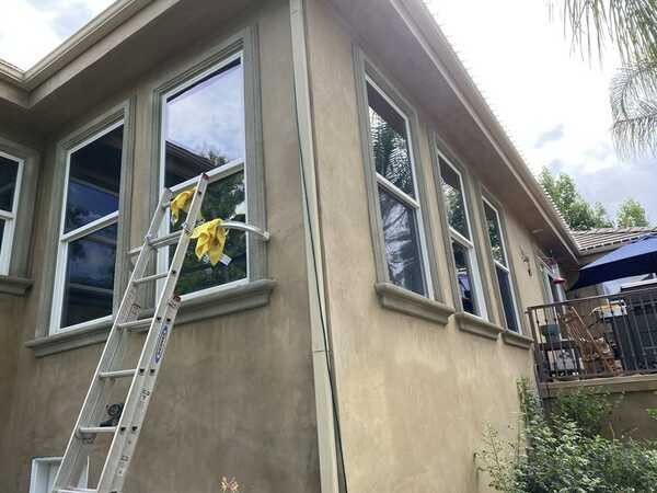 Ladder leaning against a beige house exterior below a window, with a yellow cloth hanging nearby.