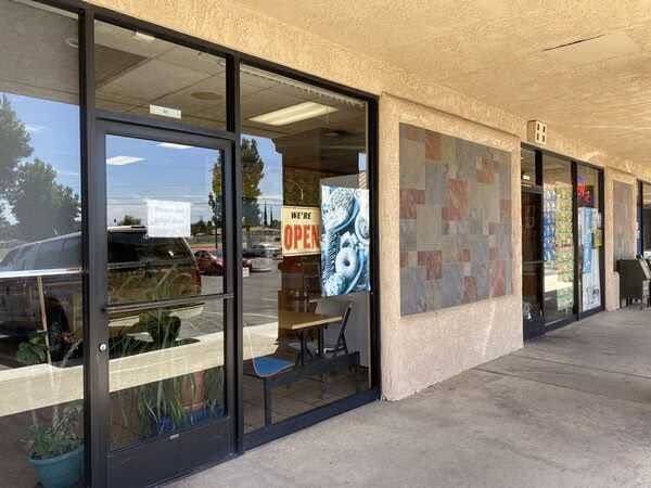 Storefront entrance with glass doors, “OPEN” sign, and blue mural panels along a covered sidewalk