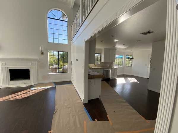Bright open living room with fireplace, tall arched window, dark wood floors, and kitchen view.