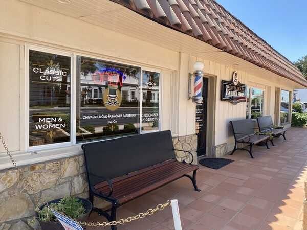 Barbershop storefront with windows, black bench, barber pole, and sidewalk seating under a tiled awning