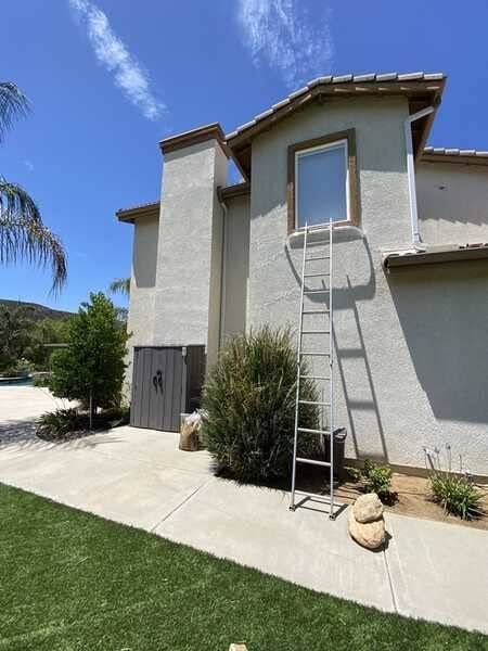 Ladder leaning against a stucco house wall beneath a second-story window on a sunny day