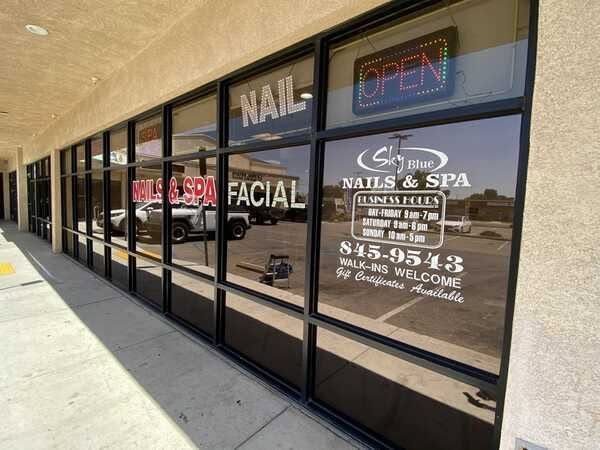 Storefront windows for a nail salon and spa with “OPEN” and service signs in the strip mall.