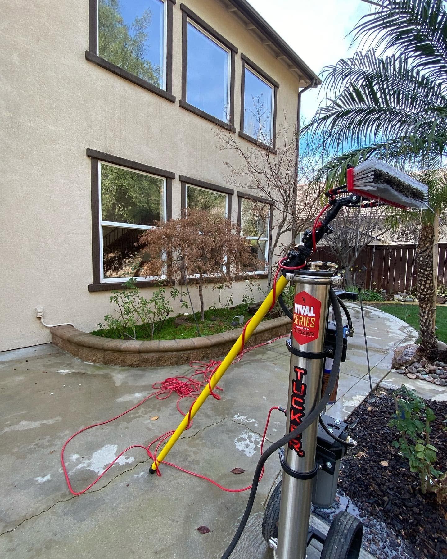 Snowy yard with a pole-mounted red-and-black utility tool beside a house and windows