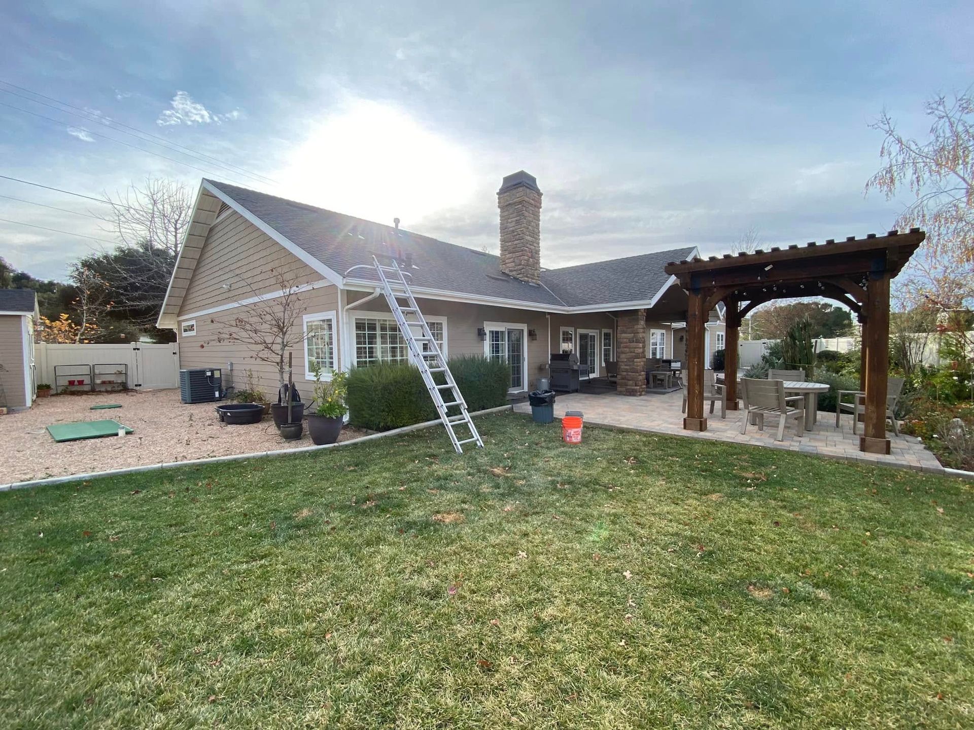 Stone house backyard with ladder, pergola, and patio under a bright sky