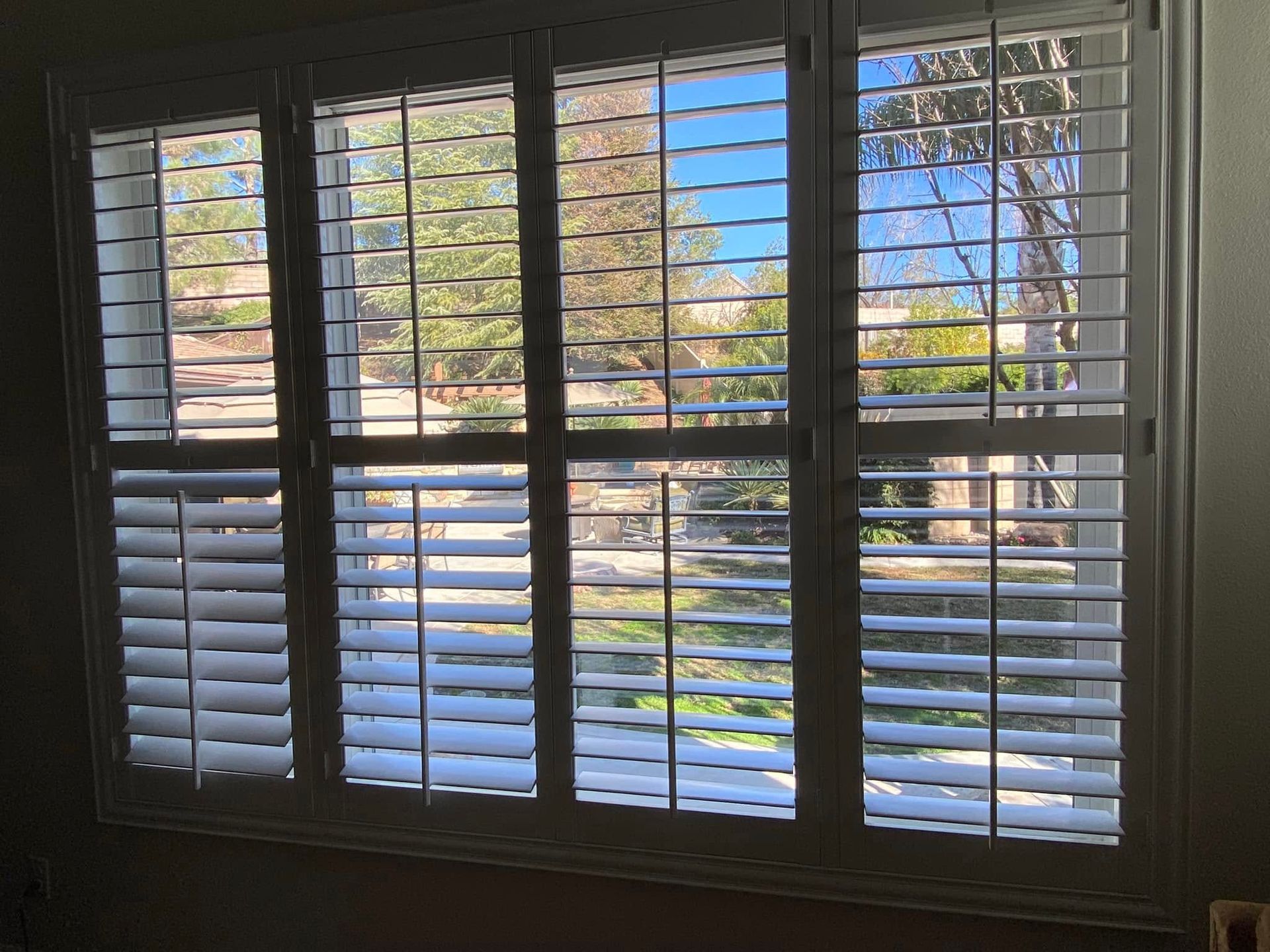 View through white window blinds to a sunny suburban street and houses outside