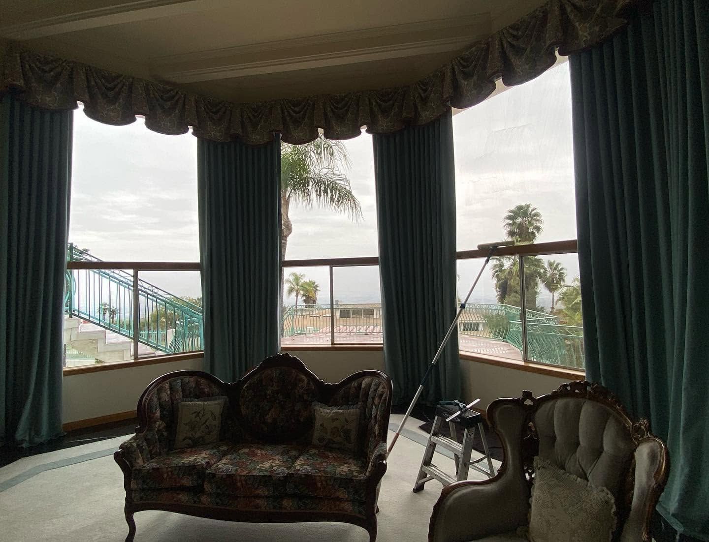 Elegant sitting room with dark drapes, patterned sofa, chairs, and a large bay window overlooking the water