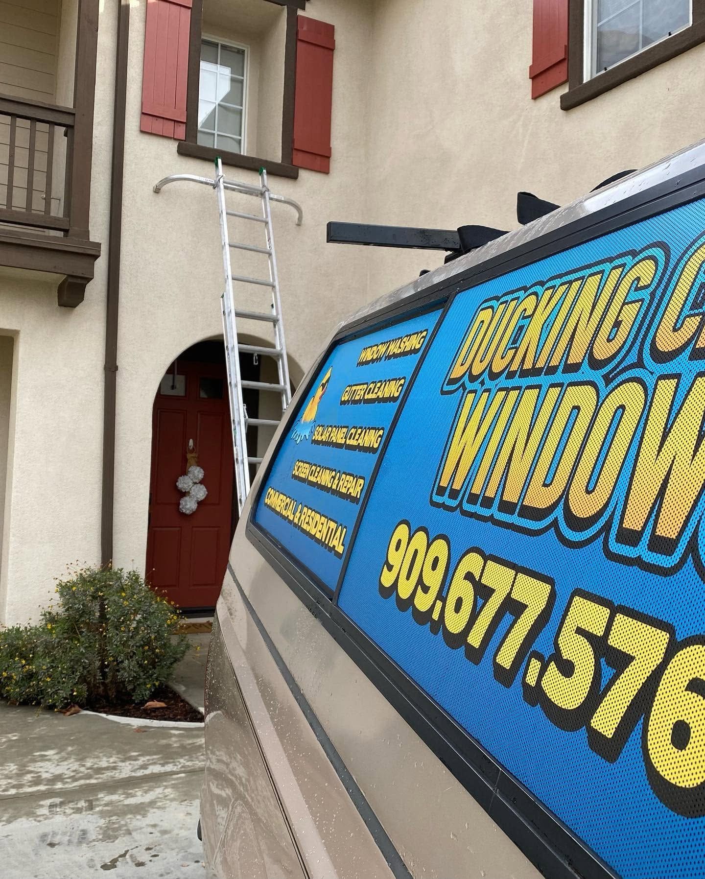 Ladder leaned against a beige building beside a red door, with a blue advertising truck in the foreground.