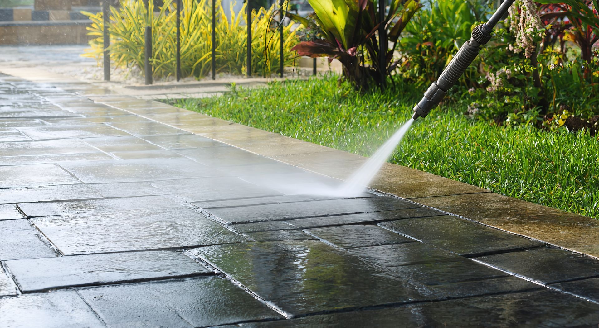 Pressure washing a wet stone walkway beside a green garden