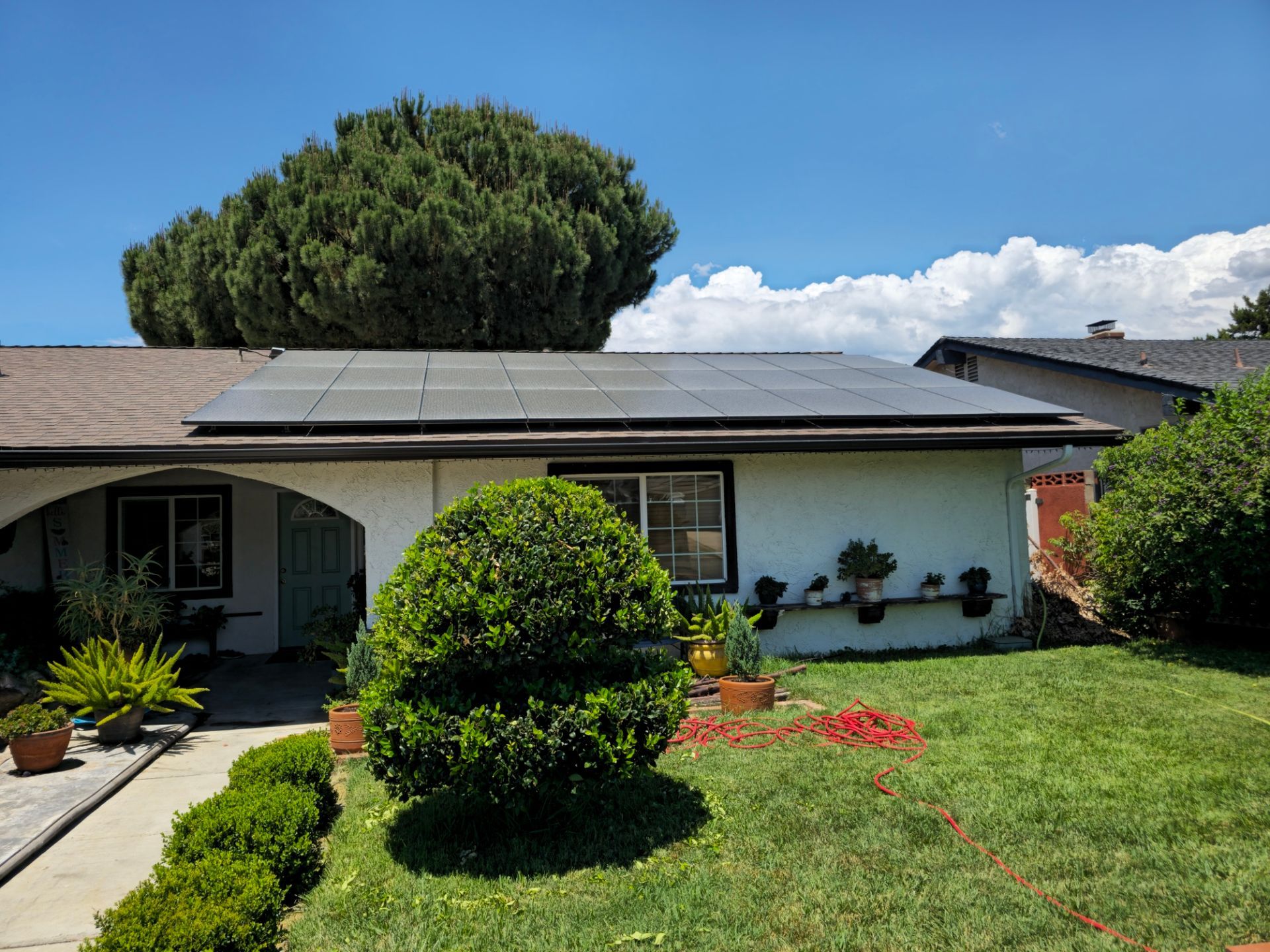 Single-story house in Calimesa, CA with solar panels, front lawn, shrubs, and a large tree under a blue sky