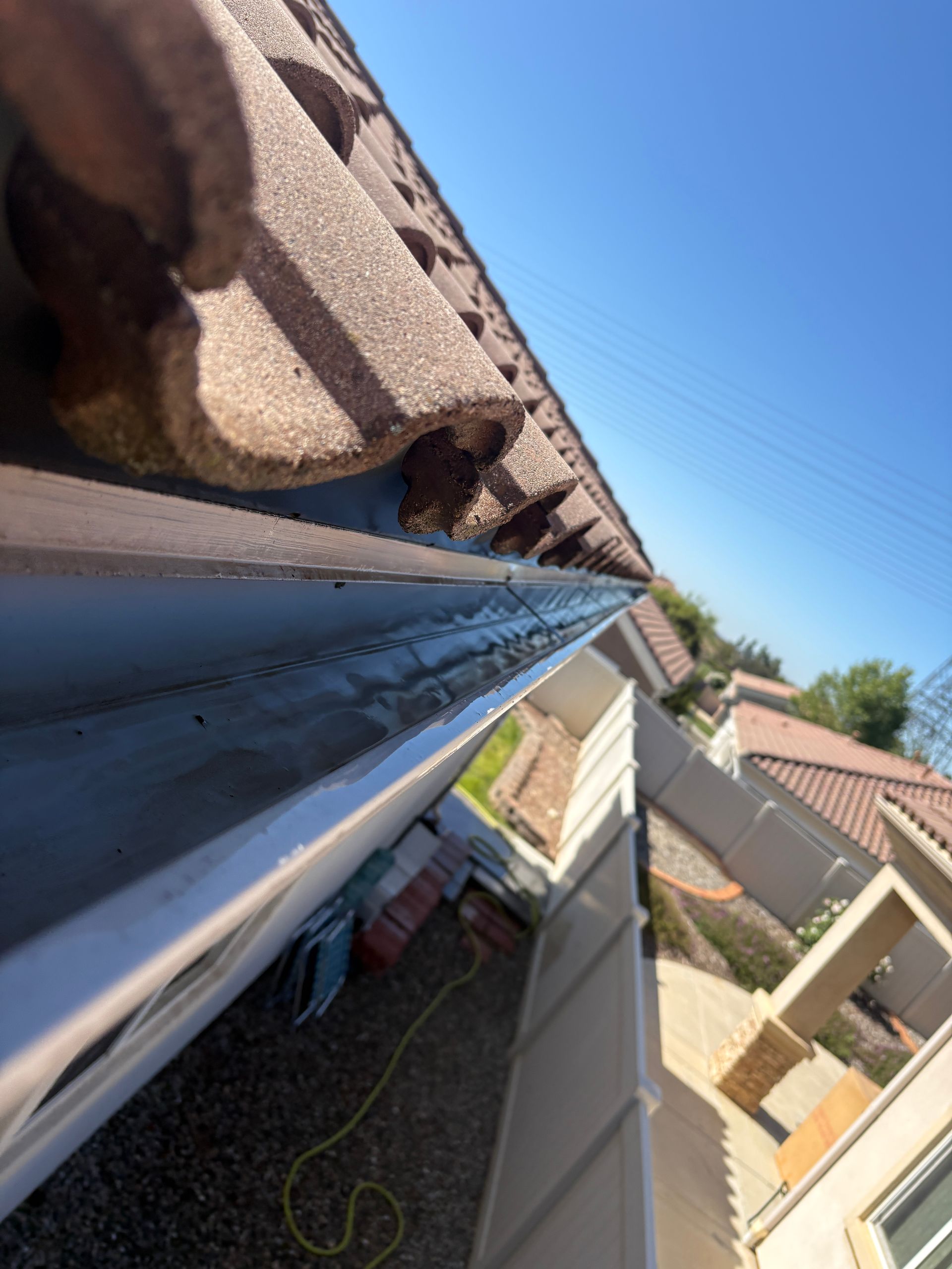 Close-up of a roof gutter along a tan tiled roof under a clear blue sky.