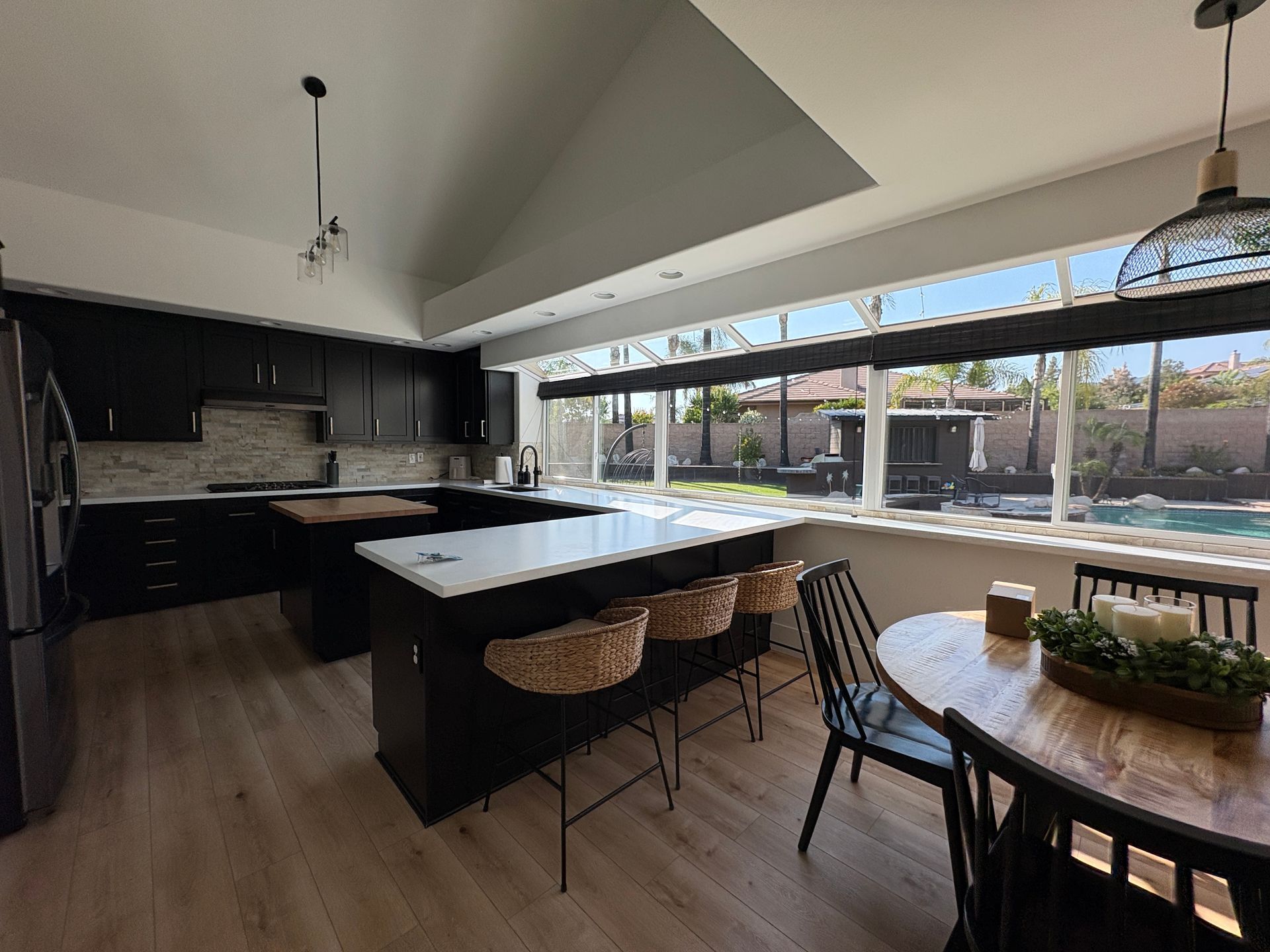 Modern kitchen with large island, bar stools, round dining table, and clean wide windows overlooking a patio