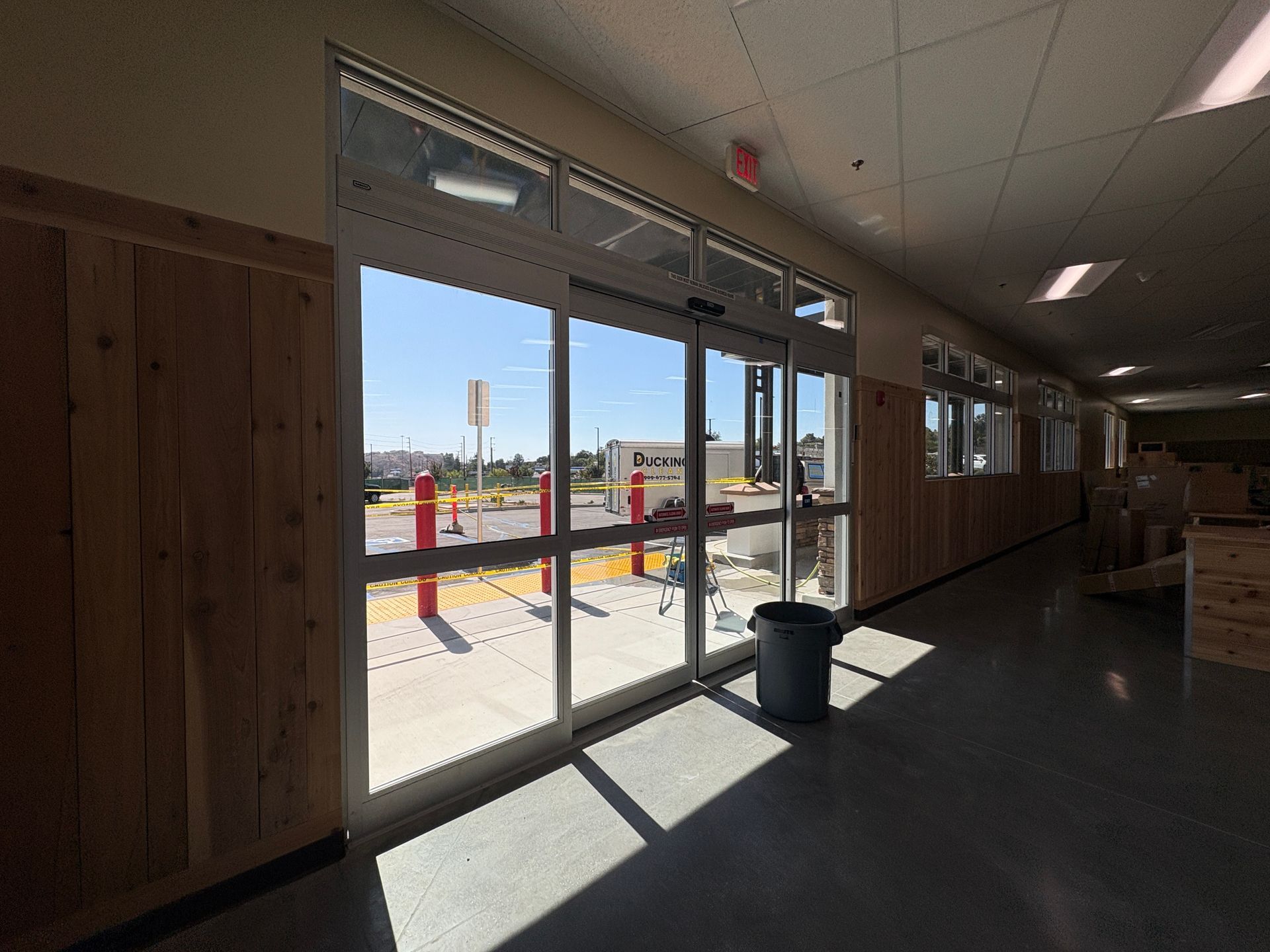 Empty hallway with clean glass doors, sunlight on the floor, and a trash can near the entrance.