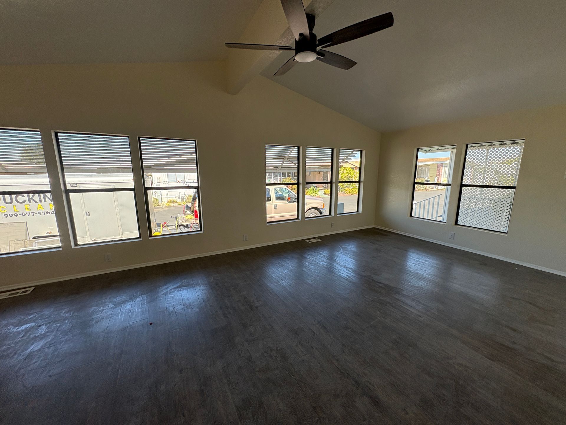Empty living room with dark wood floors, ceiling fan, and cleaned large windows overlooking a yard