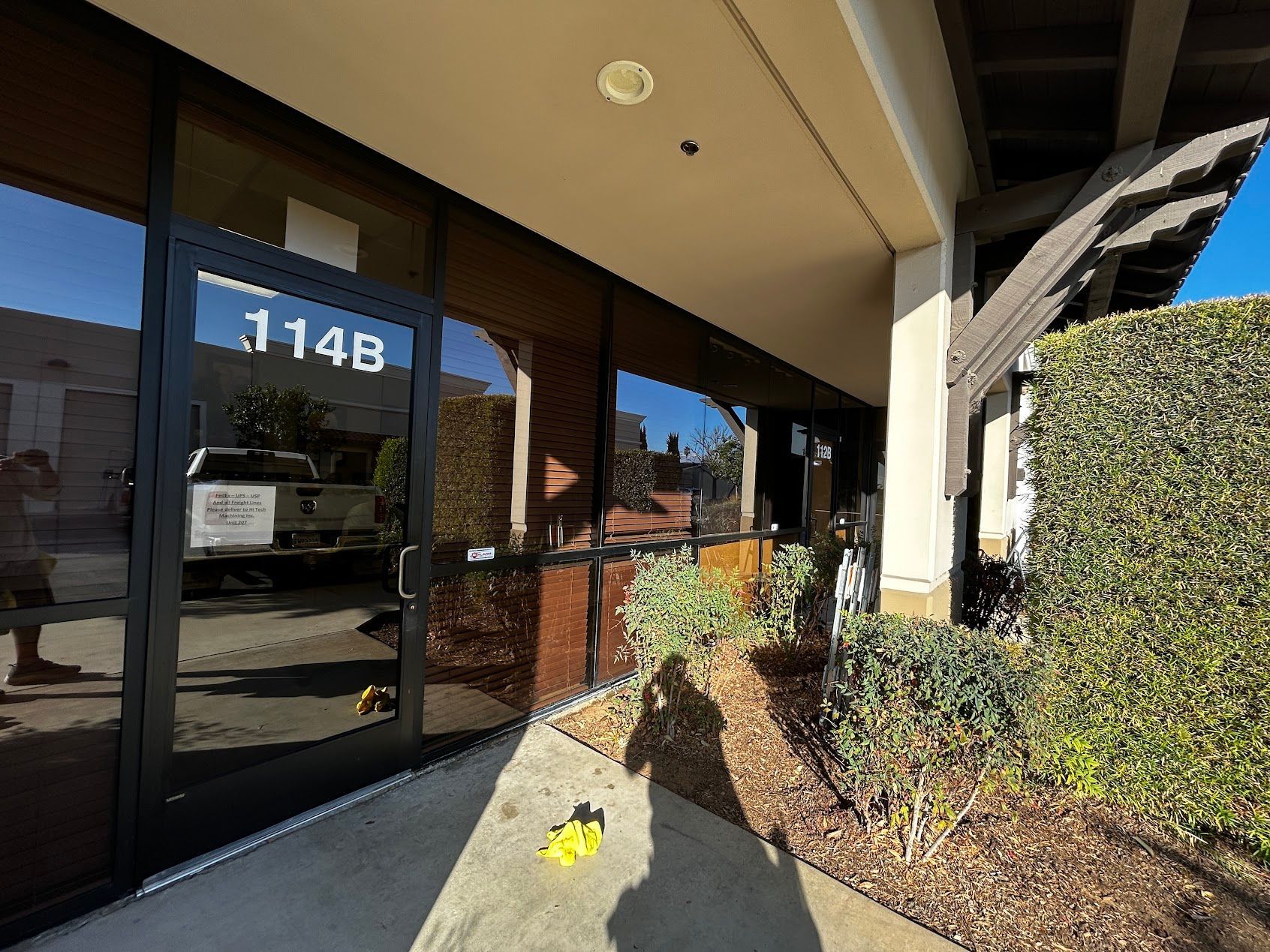 Building entrance with glass doors marked 1148, bordered by a hedge and landscaped walkway.
