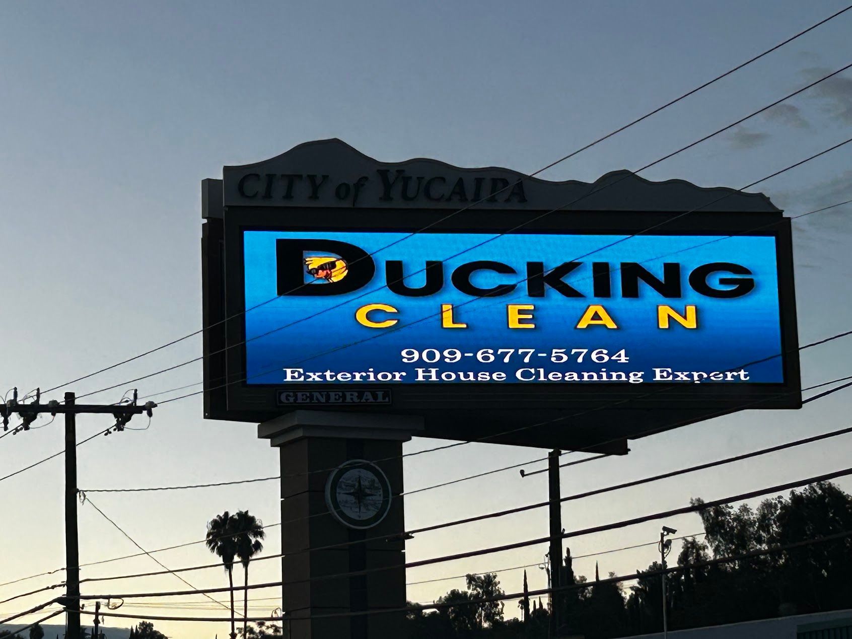 Bucking Clean cleaning service billboard in Yucaipa at dusk, blue and black sign by power lines