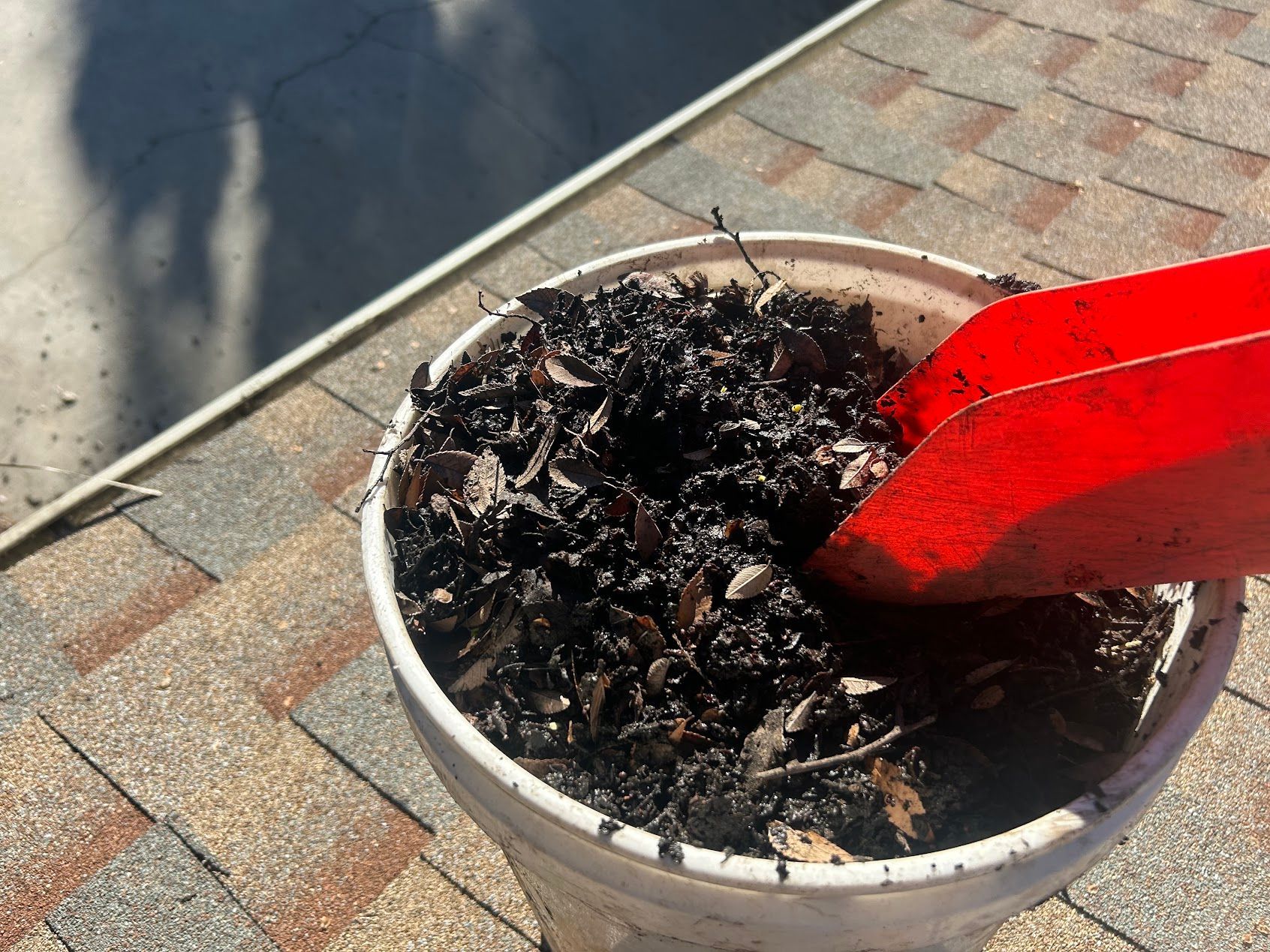 Red shovel in a white pot of dark soil on a brick patio