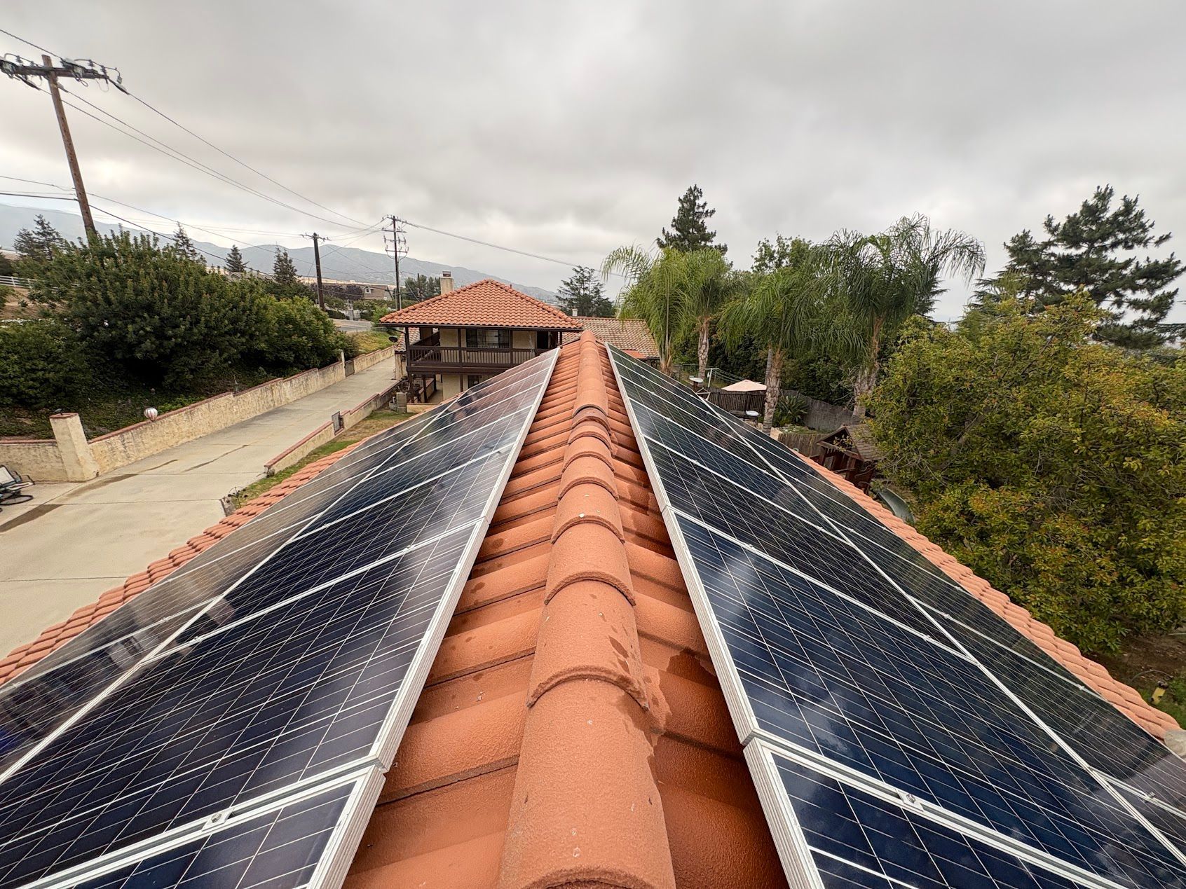 Solar panels on a terracotta-tiled roof in a rural neighborhood under a cloudy sky