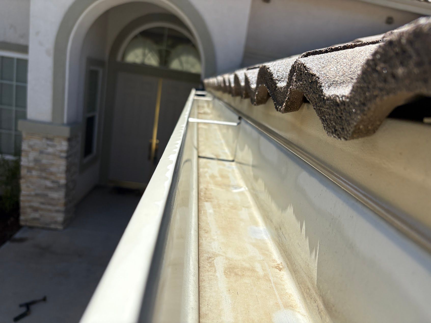Close-up of a house gutter along a roof edge beside an entryway and stone siding.