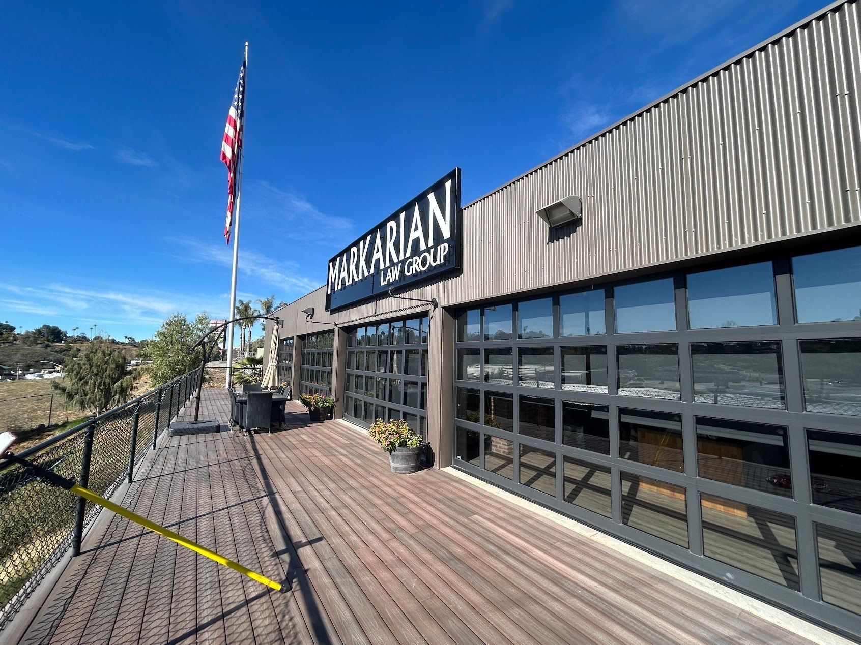 Exterior of a restaurant with a wooden deck, large windows, and an American flag under a blue sky
