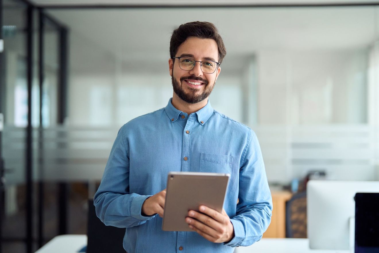 Smiling person in a blue shirt holding a tablet in a bright office