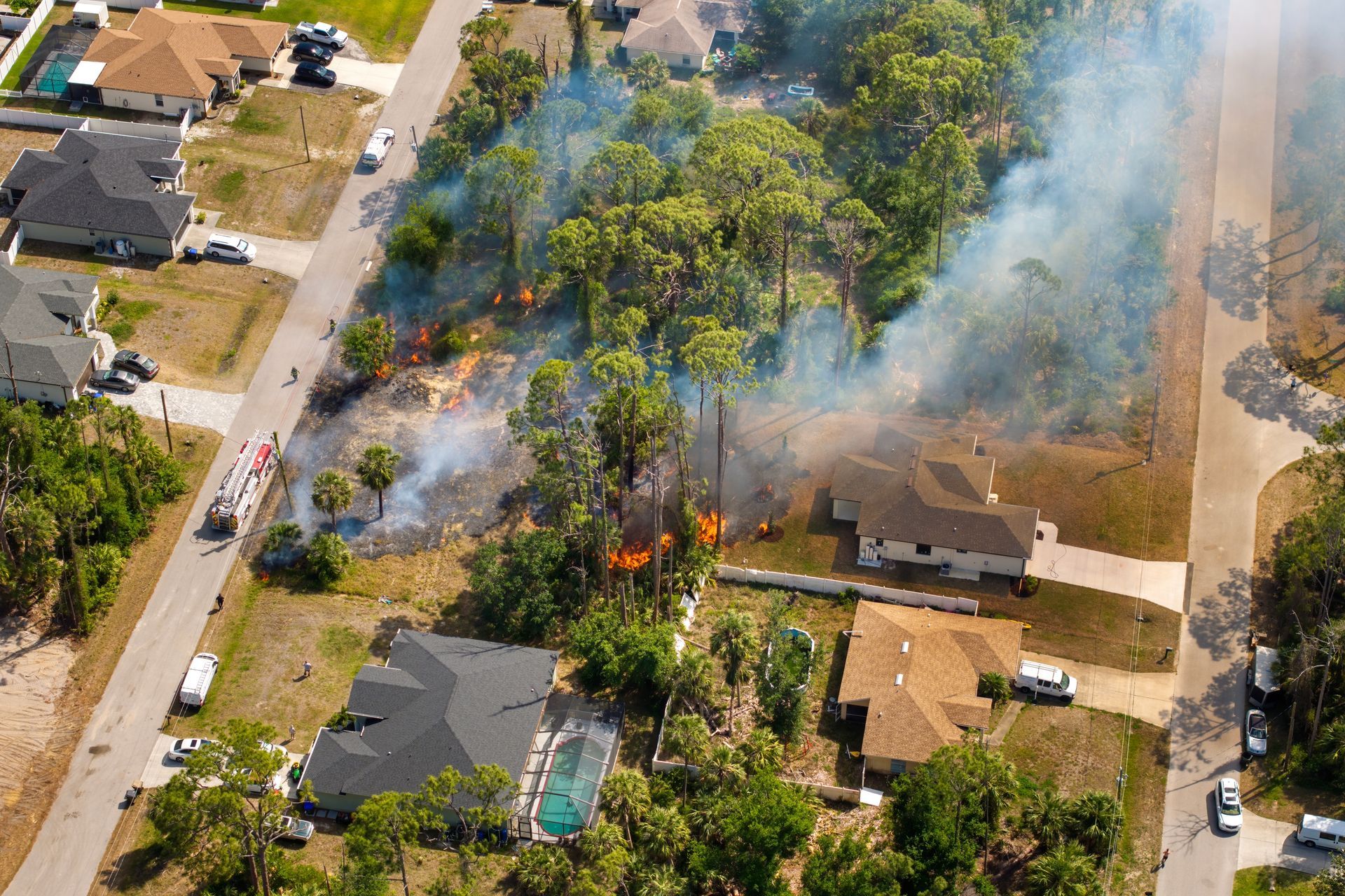 Aerial view of a suburban house fire with smoke and flames near nearby homes and trees
