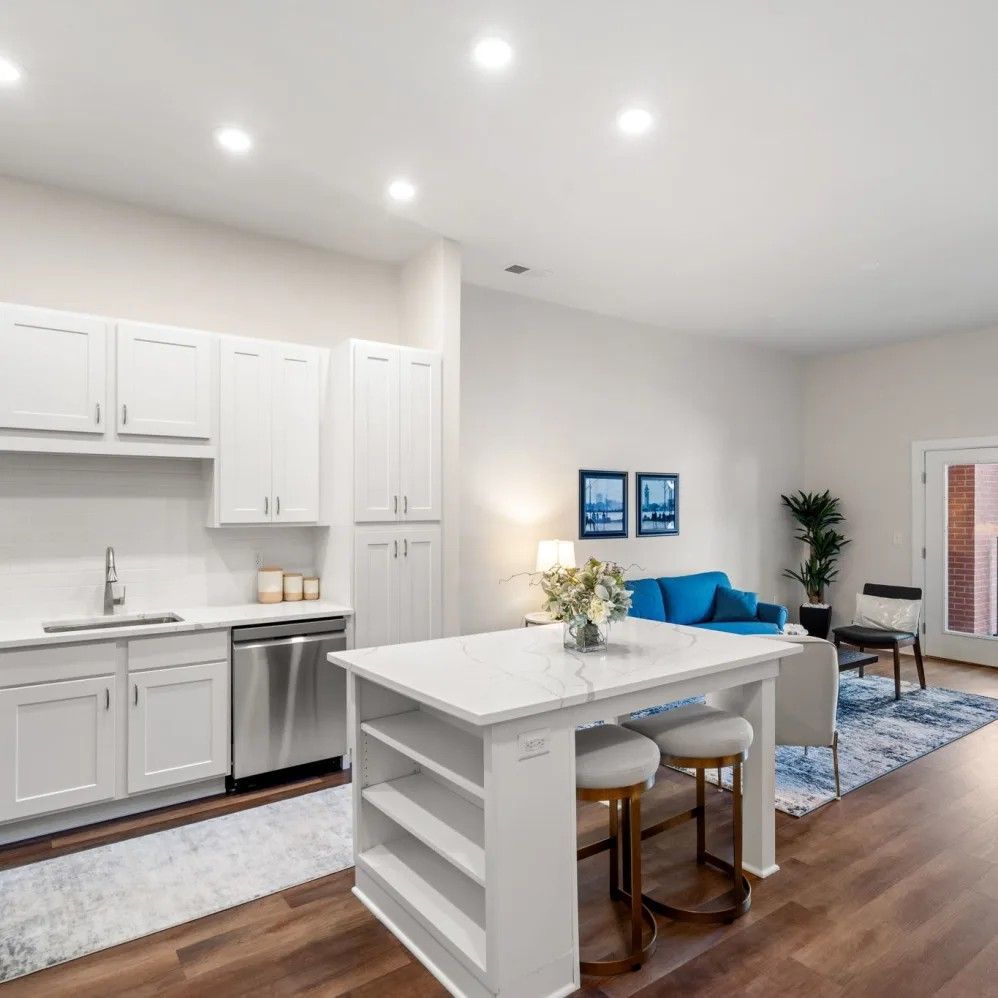 White kitchen with island, stainless steel appliances, open to living room with blue sofa, hardwood floors.