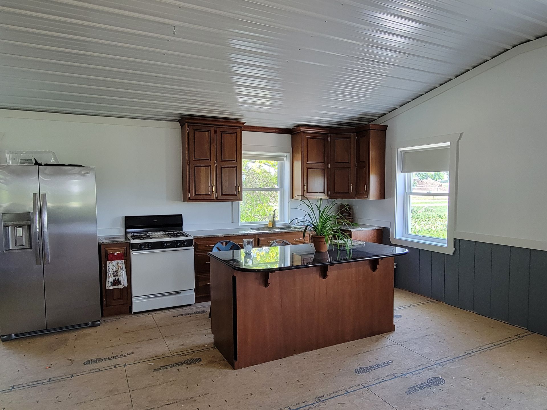 Kitchen with stainless steel fridge, stove, island, and wood cabinets. Light-colored flooring and white walls.