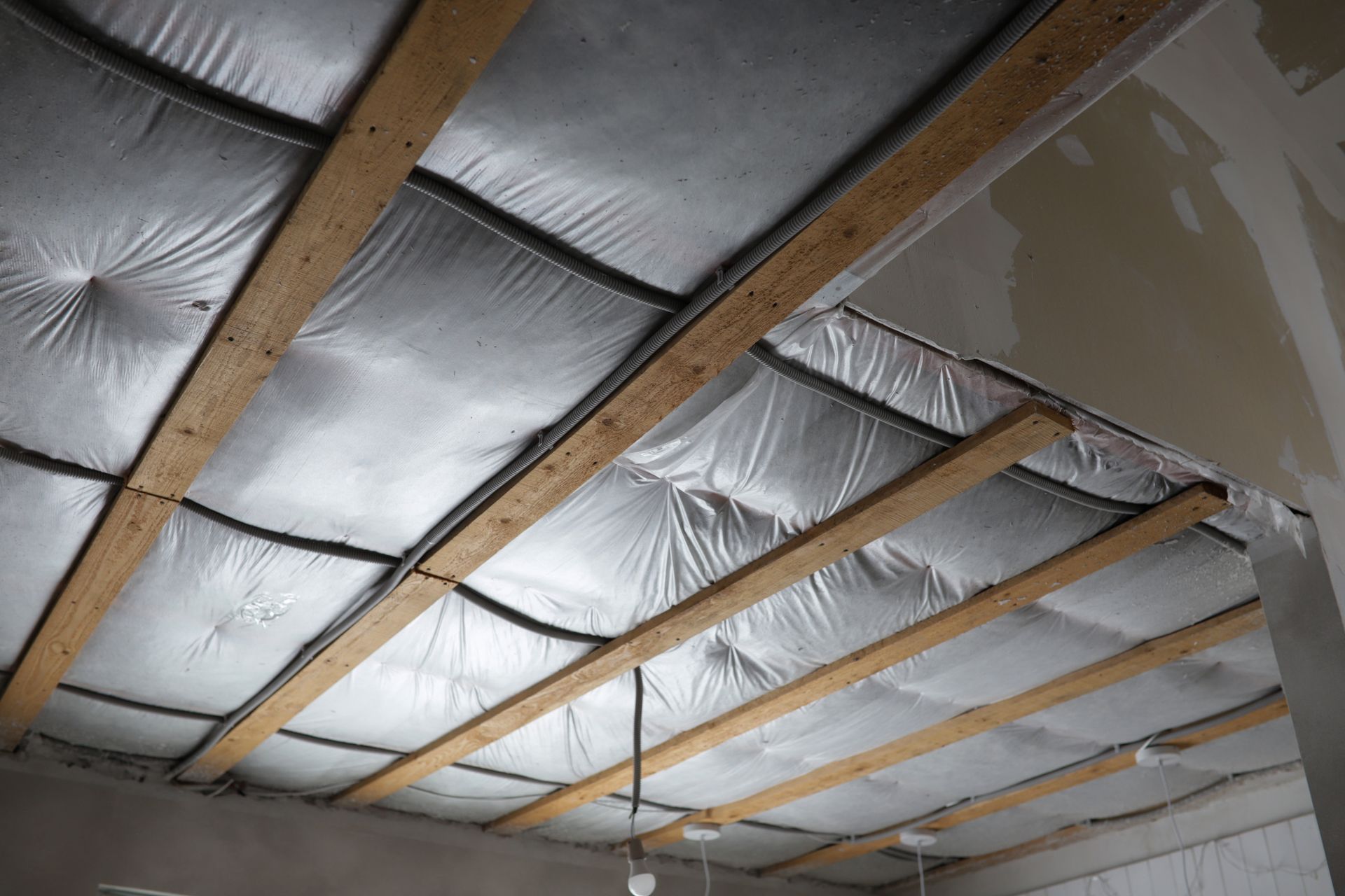 Partially insulated ceiling with exposed wooden rafters and unfinished drywall panels