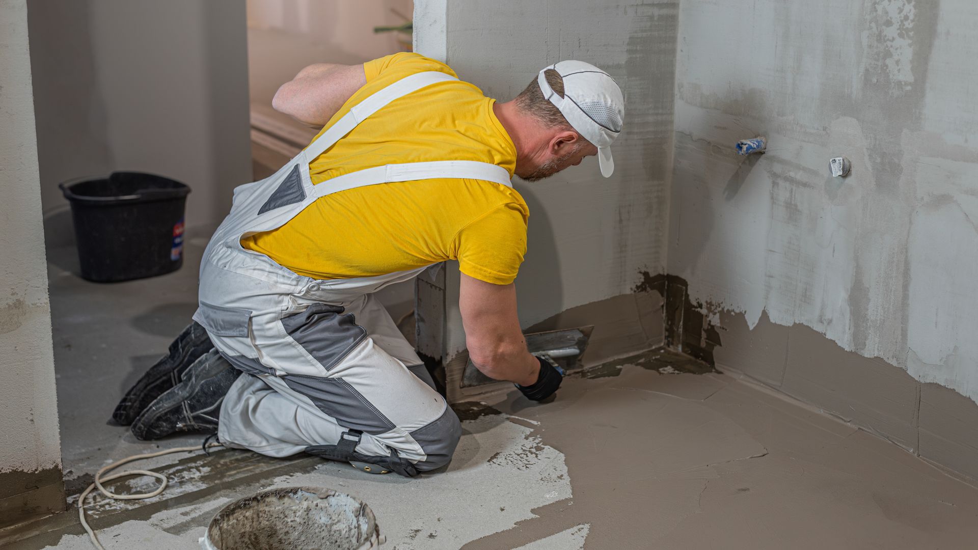 Construction worker kneeling and using a tool to fix a wall floor joint in an unfinished room