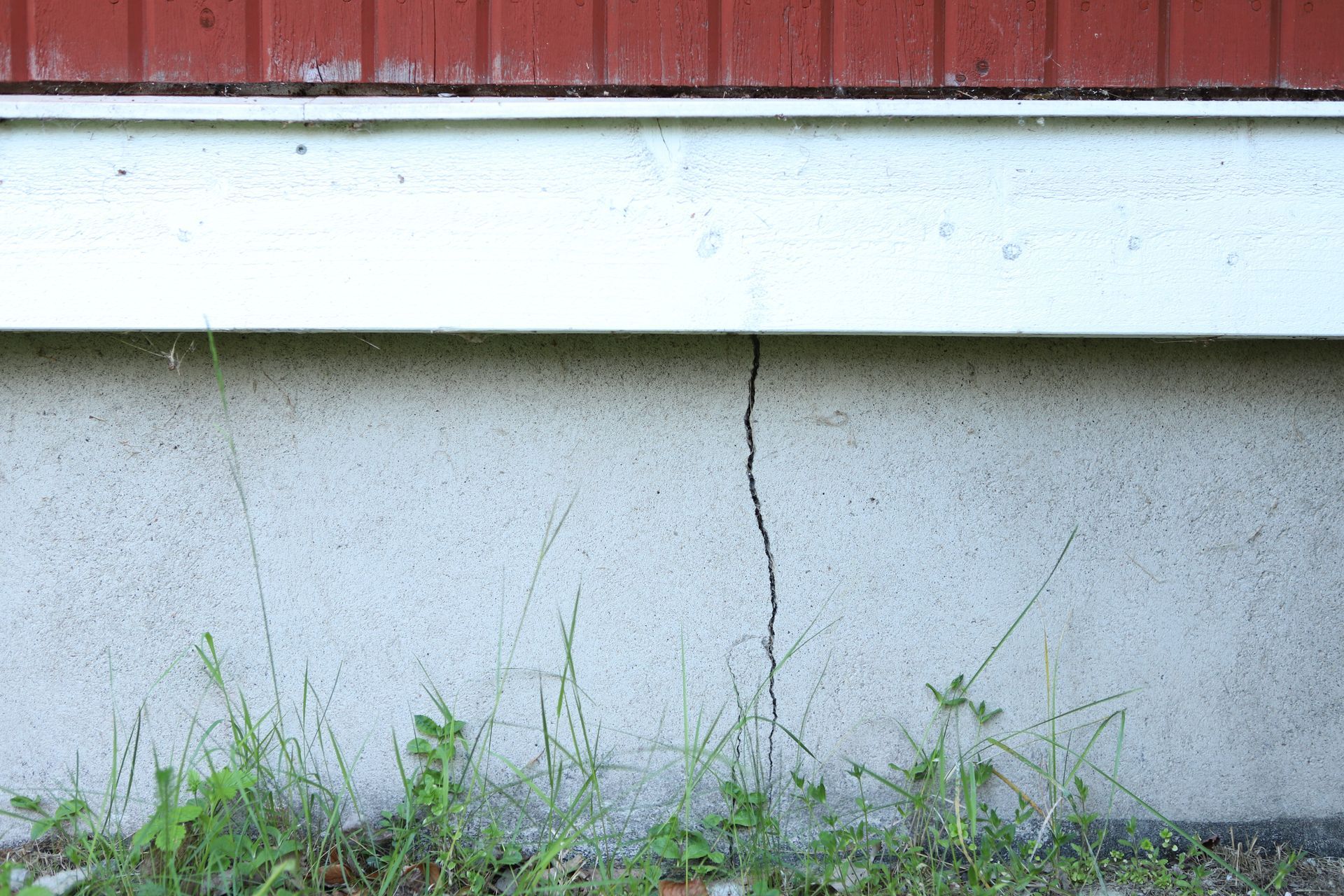 Cracked concrete wall below a white ledge, with grass growing at the base