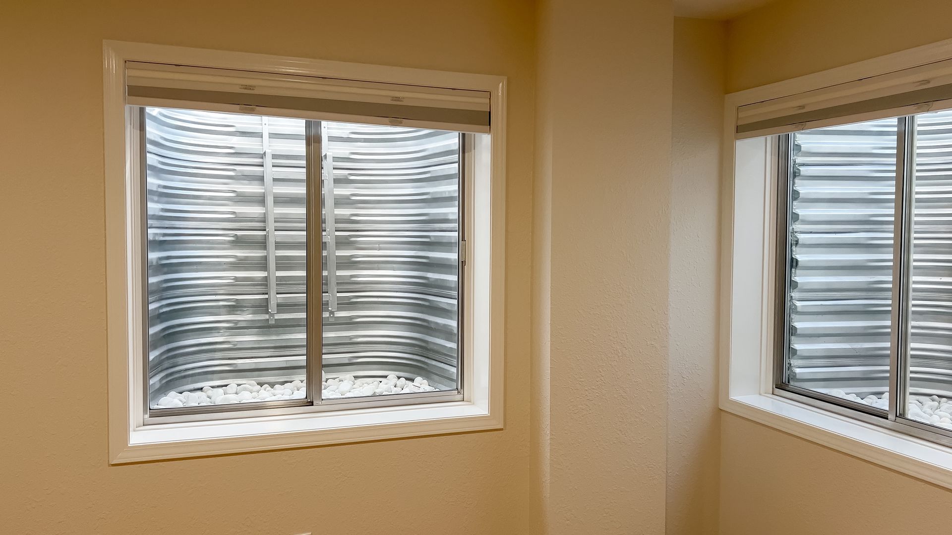 Two windows with white blinds on beige walls in a sunlit room