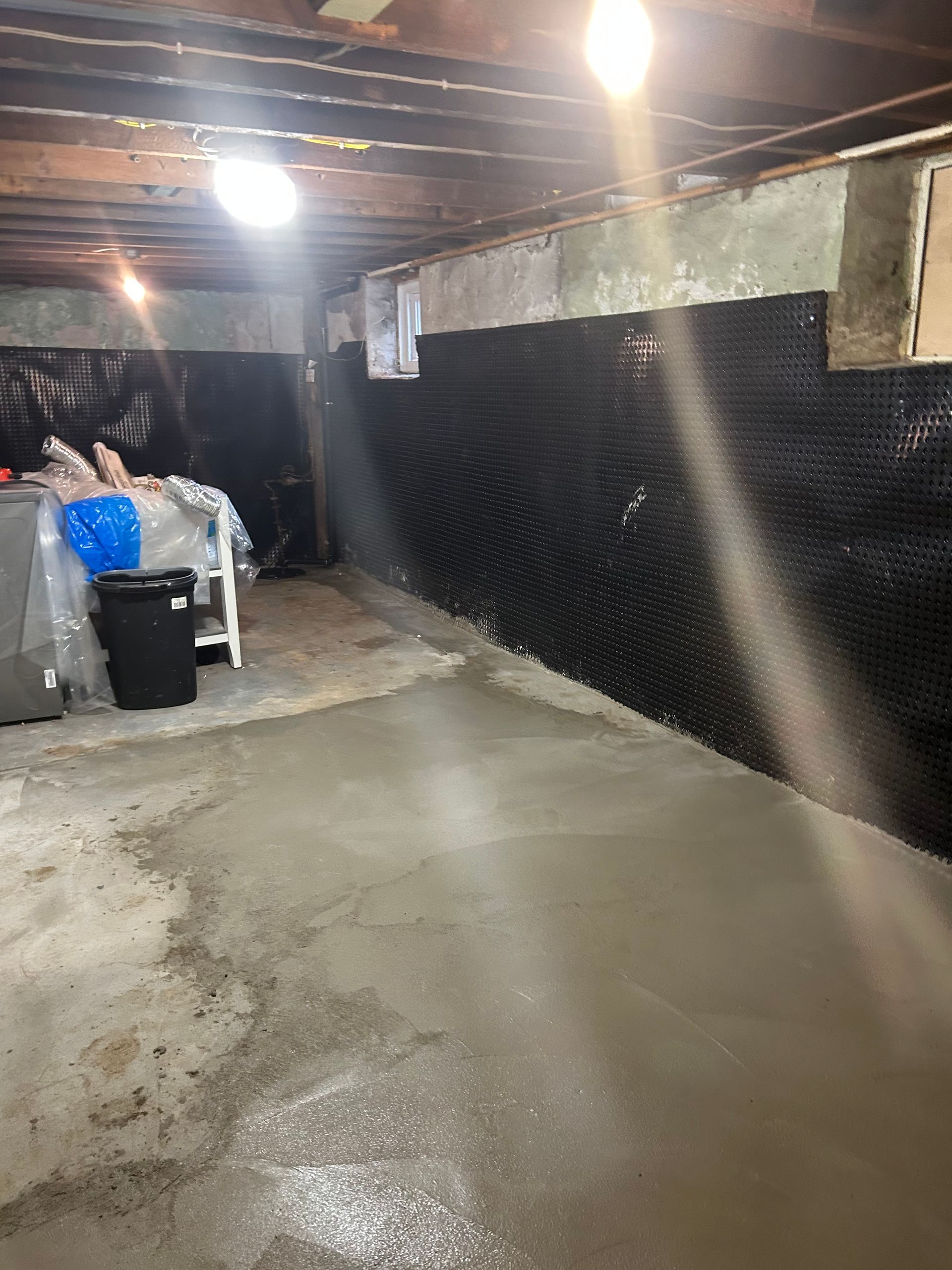 Basement with new concrete floor; black drainage membrane on walls.