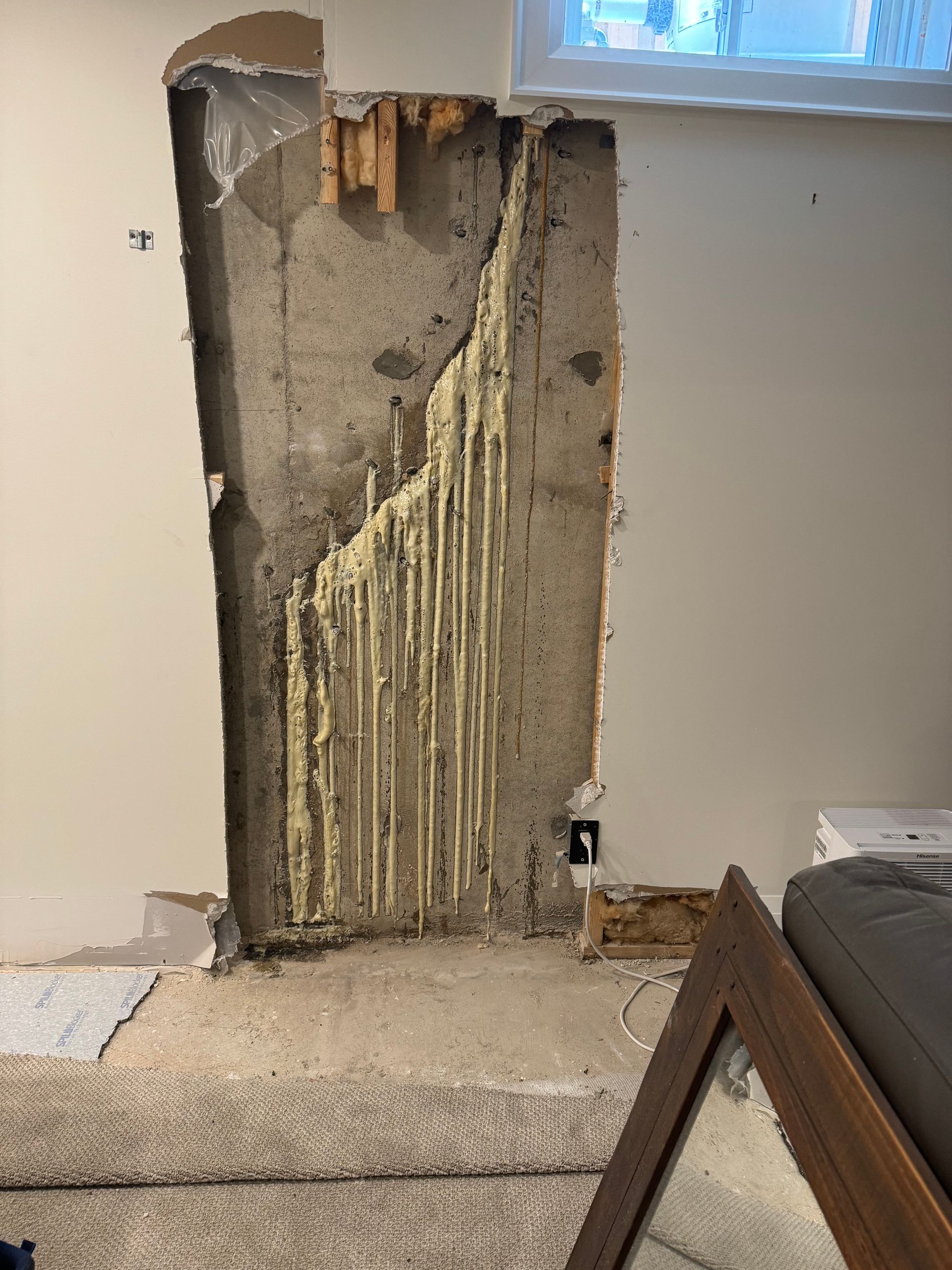 Concrete wall with foam insulation exposed, partial drywall removal, interior setting.