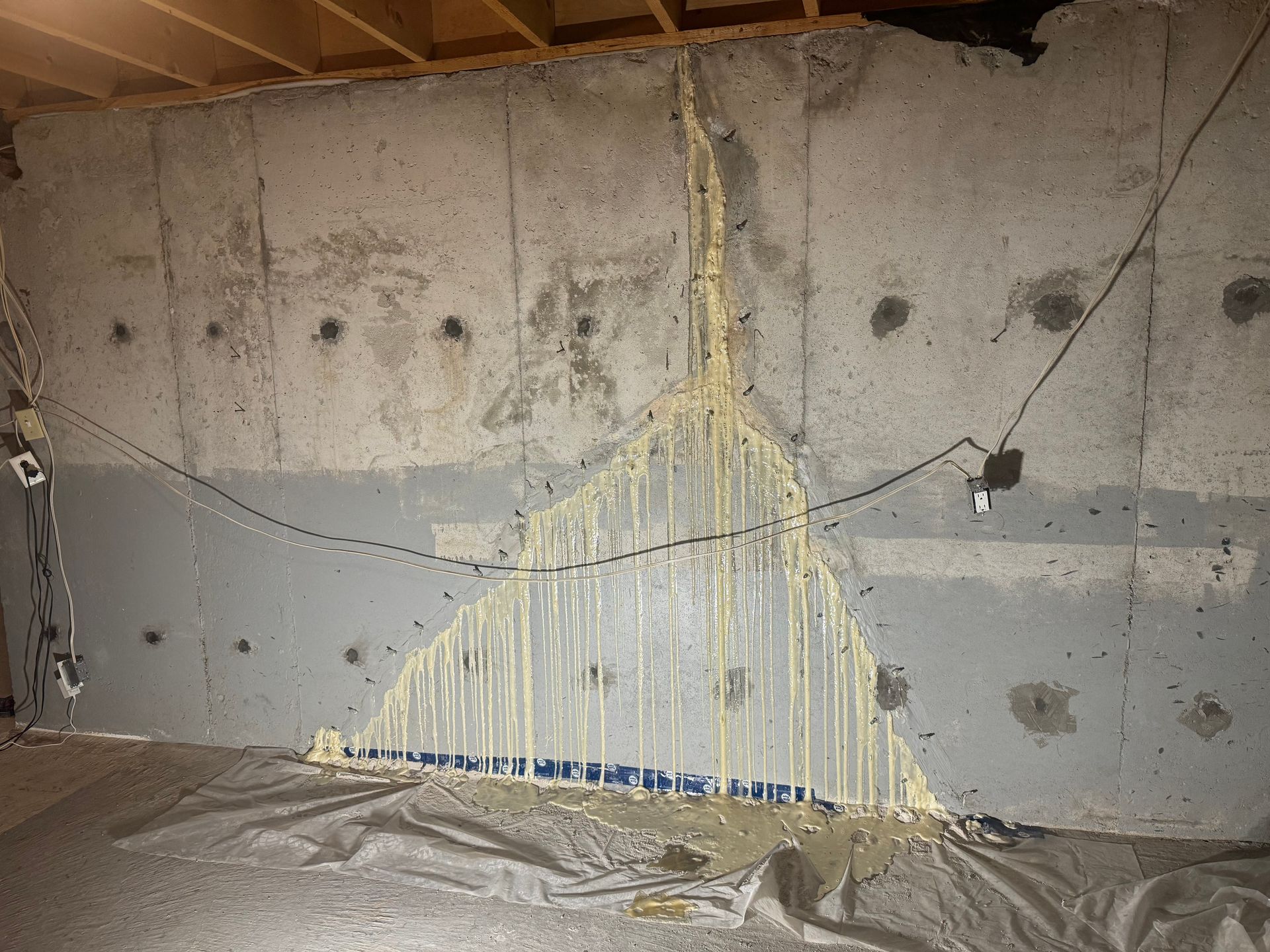 Concrete basement wall with a large crack filled with yellow sealant, drips downward.