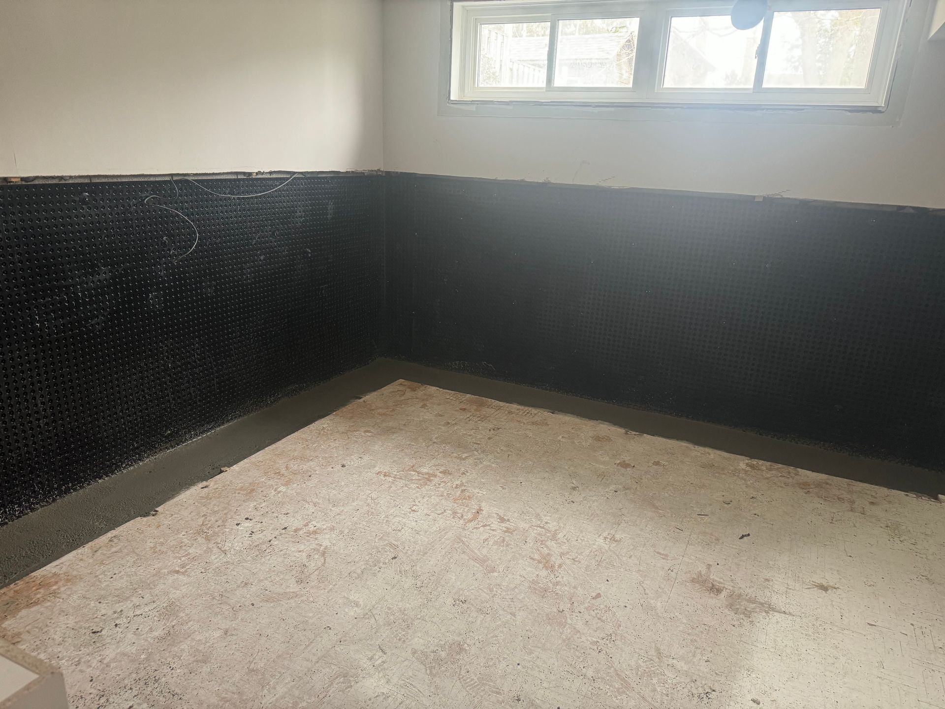 Corner of a room with black dimpled wall covering, concrete floor, and window.