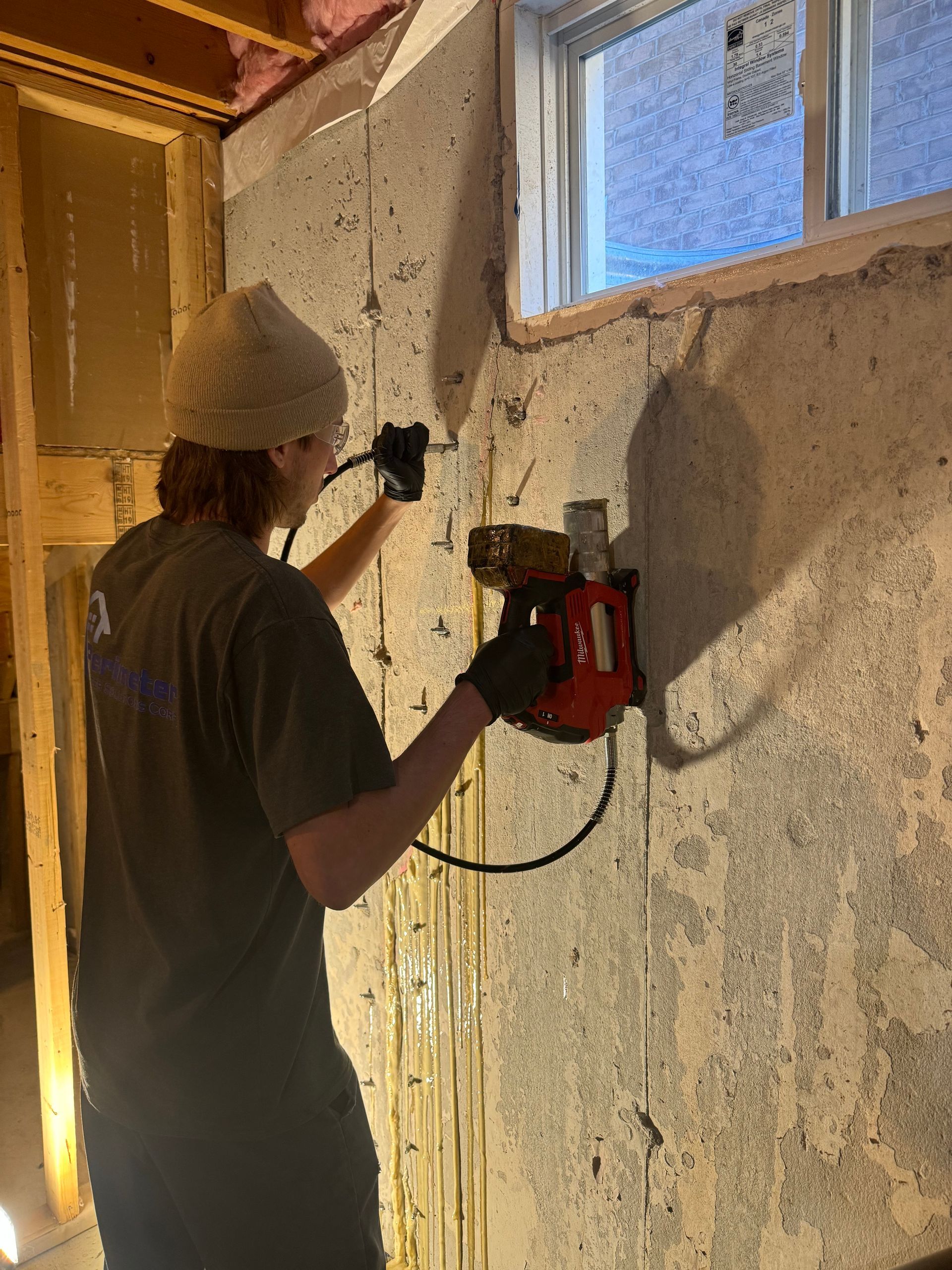 Person using a red saw to cut into a concrete wall near a window in a basement.