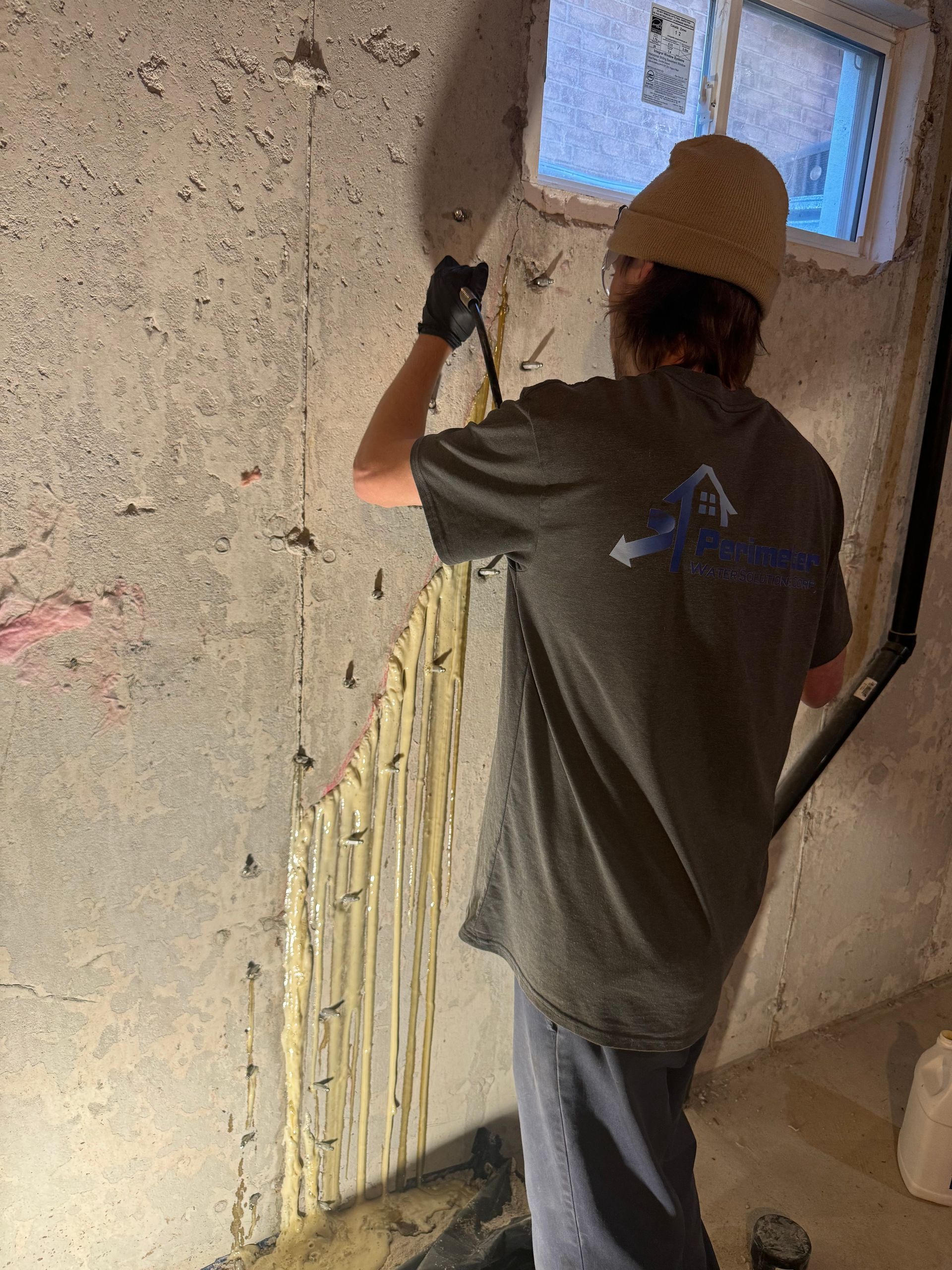 Person applying sealant to a concrete basement wall near a small window.
