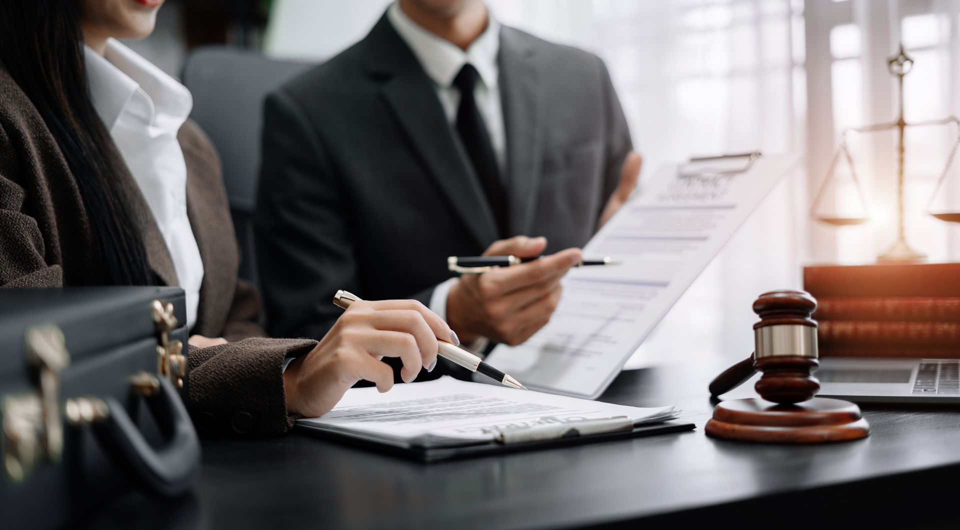 Two lawyers reviewing documents, gavel and scales of justice on desk.