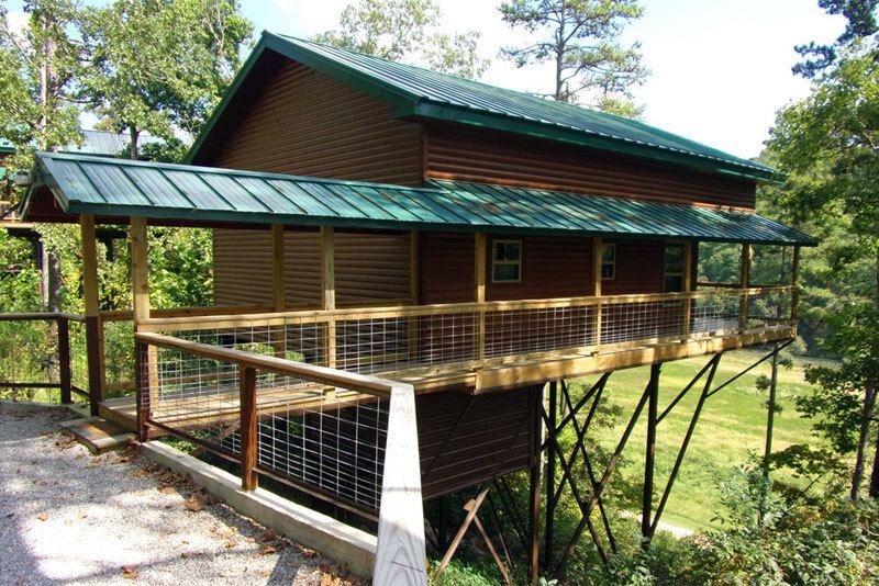 Wooden cabin on a raised deck with a green metal roof in a wooded area