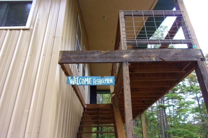 Wooden staircase and balcony beside a beige building, with a blue “Welcome” sign hanging underneath.