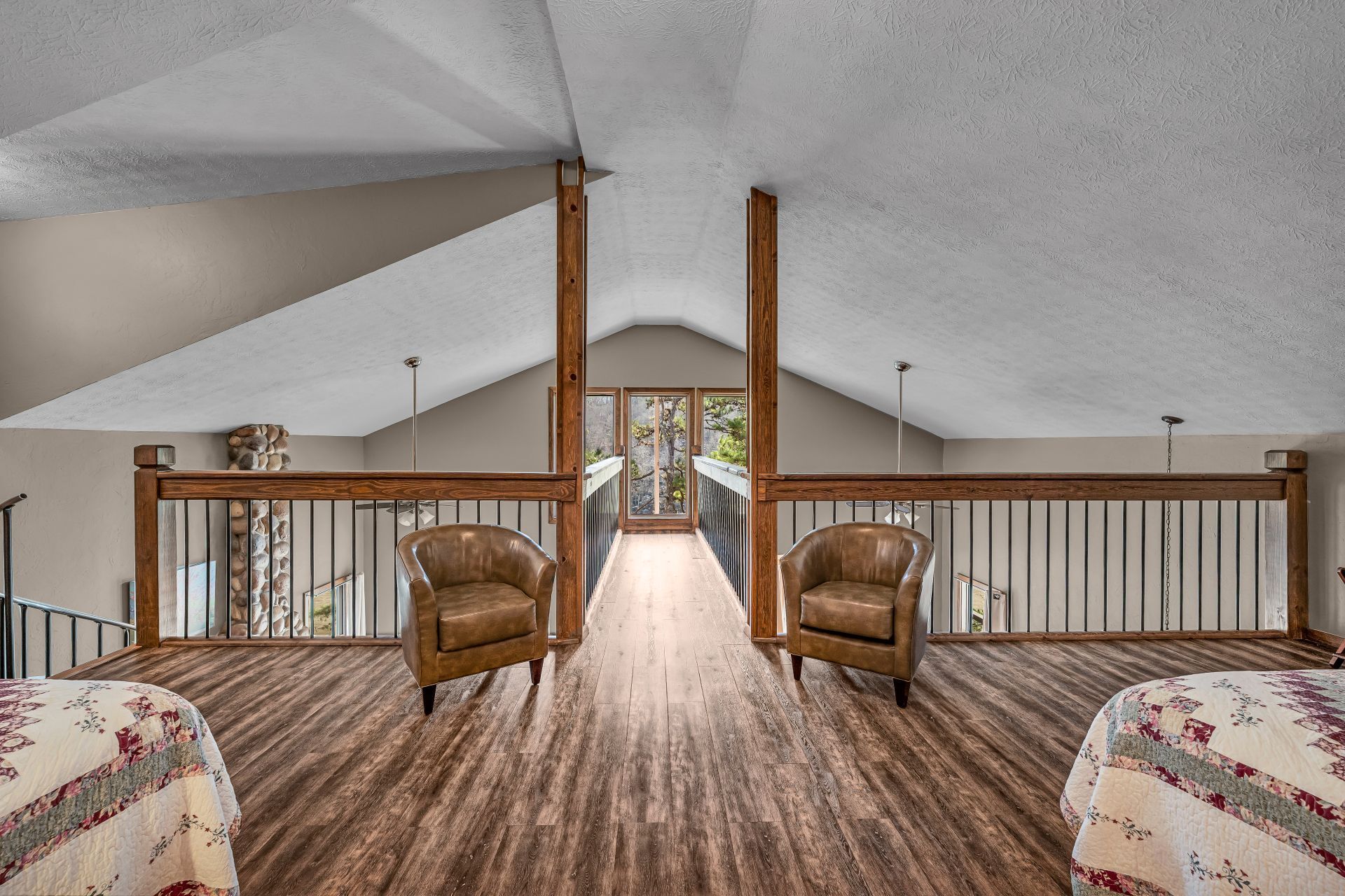 Loft bedroom with wood floors, two armchairs, and a cathedral ceiling overlooking a lower level.