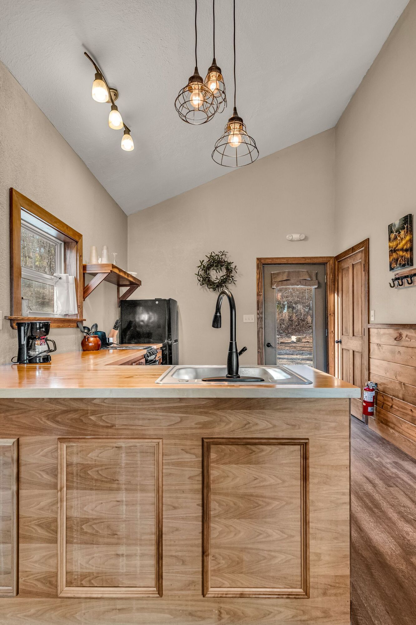 Modern kitchen with light wood cabinets, high ceiling, pendant lights, and a black coffee maker on the counter