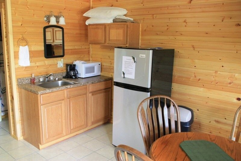 Small wood-paneled cabin kitchenette with sink, microwave, mini fridge, and dining table