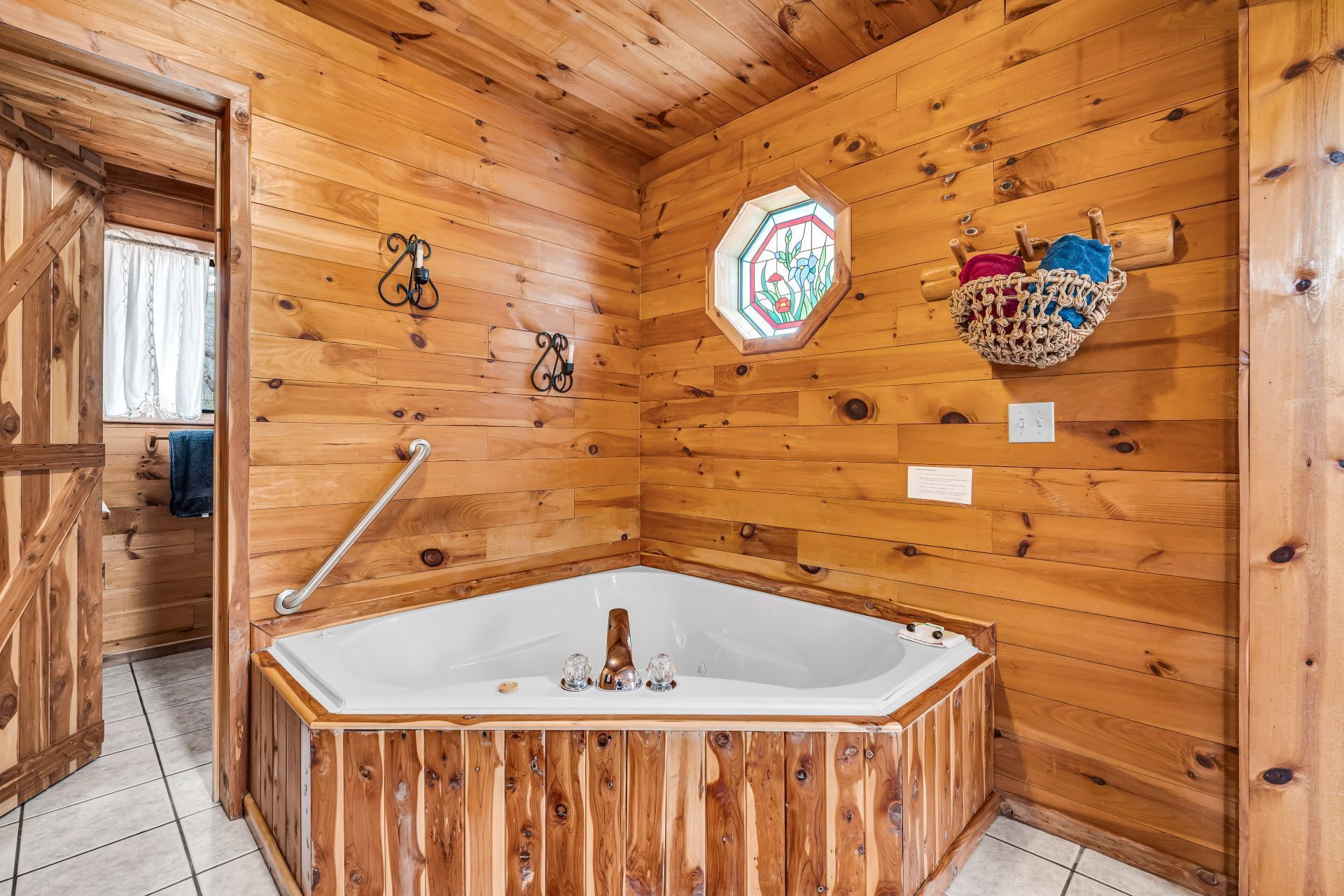 Wood-paneled bathroom with a corner jacuzzi tub, stained glass window, and tiled floor