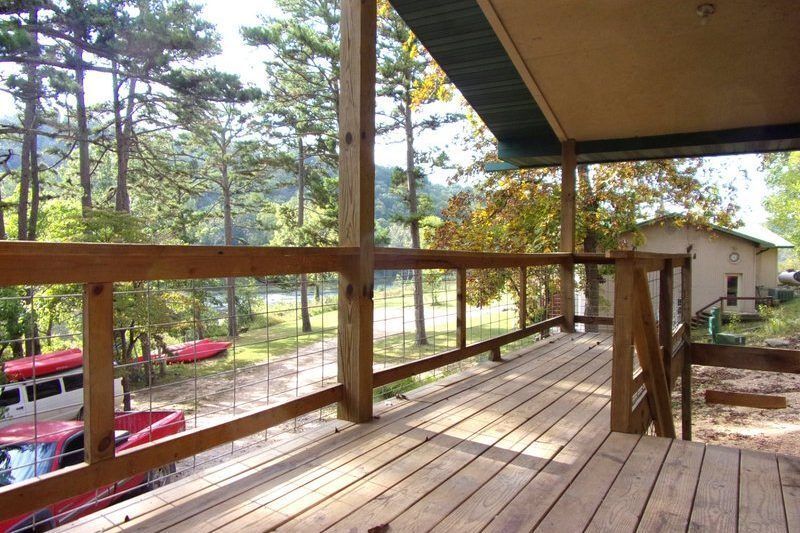 Wooden porch with railing overlooking trees and parked cars near a small building