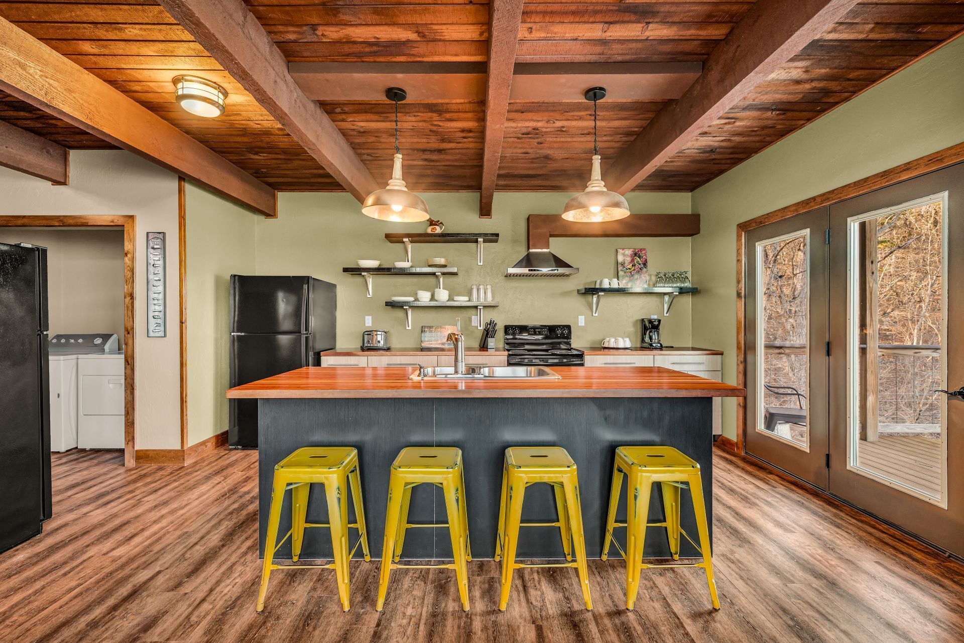 Rustic kitchen with wood beams, black island, yellow stools, and large windows