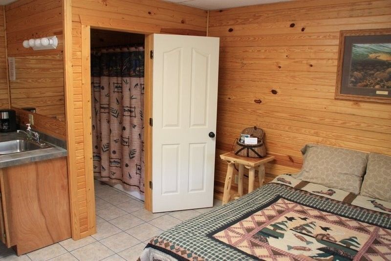 Wood-paneled bedroom with bed, bedside table, open door, and adjoining bathroom visible