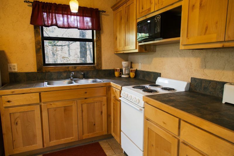 Small kitchen with wooden cabinets, white stove, dark countertops, and a window above the sink.
