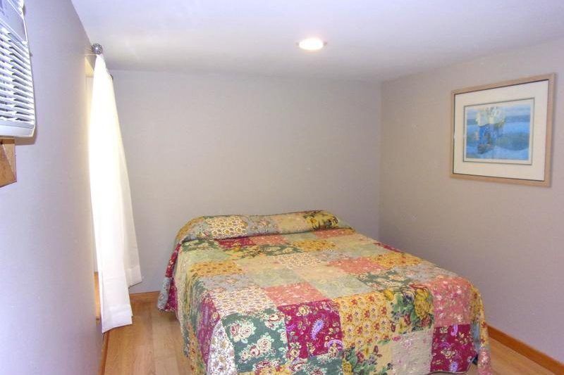 Small bedroom with a colorful quilted bed, window, recessed lights, and framed wall art.
