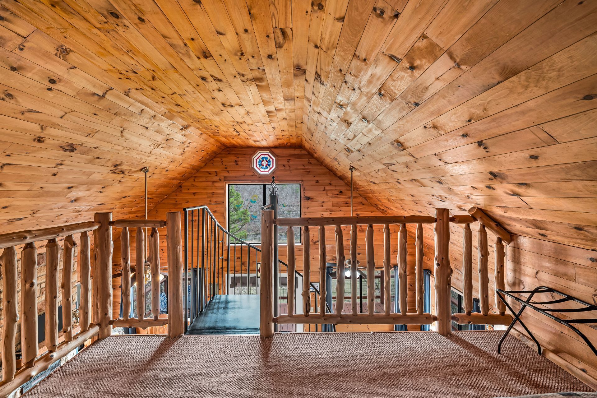 Wood-paneled loft with a wooden railing, open doorway, and view of the outdoors